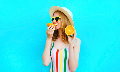 Summer portrait happy woman holding in her hands and eating slices of orange fruit in straw hat on colorful blue background