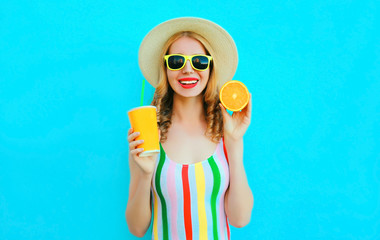 Summer portrait happy smiling woman holding in her hands cup of fruit juice, slice of orange in straw hat on colorful blue background