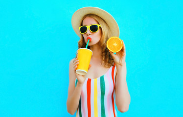 Summer portrait woman drinking fruit juice holding in her hand slice of orange in straw hat on colorful blue background