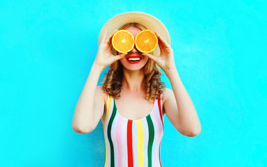 Summer portrait happy smiling woman holding in her hands two slices of orange fruit hiding her eyes in straw hat on colorful blue background