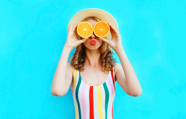 Summer portrait woman holding in her hands two slices of orange fruit hiding her eyes in straw hat on colorful blue background