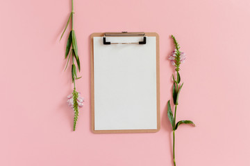 Flatlay of clipboard mockup and wildflowers on a pink background