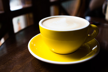 Yellow cup of aromatic coffee on a wooden table.
