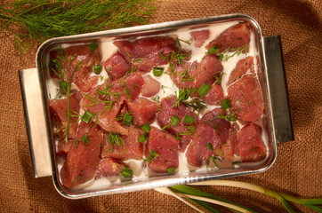 Marinated in milk and herbs, the meat in a steel pot on the cloth with fresh herbs