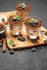 Classic tiramisu dessert in a glass with blueberries on dark concrete background