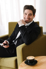 Confident handsome man wearing suit sitting in armchair