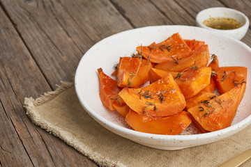 roasted pumpkin, pieces in plate with honey and seasonings, old rustic wooden dark table, copy space, side view