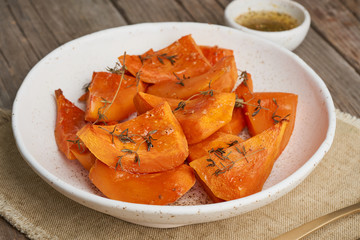 roasted pumpkin, pieces in plate with honey and seasonings, old rustic wooden dark table, side view,