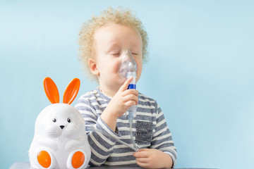Sweet little boy having inhalation for easy cough on blue background. Allergy and health care concept. Copy space