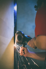 A man repairs a door in the basement of his house using a manual grinding machine.