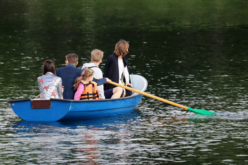 Family rides on a rowing boat on a summer lake. Parents with children traveling and having fun together, leisure on a water