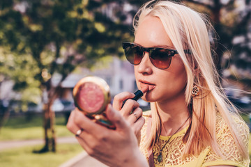 Beautiful blond womam looking in a small mirror and coorect her lipstick.