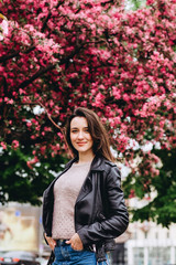 Obraz na płótnie Canvas Outdoor portrait of young beautiful fashionable lady posing near flowering tree. Female beauty fashion. City lifestyle. girl in yellow cardigan on a background of pink flowering trees. Girl smiling