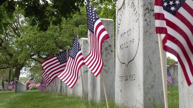 Close up side view of gravestones in a cemetery of civil war soldiers remains on Memorial day with American flags flapping in the wind