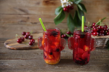 sweet compote of fresh berries and fruits in a glass jar with a straw for drinking with fresh berries of sweet cherry in a basket on a table made of natural wood. Fresh summer drink. With copy space.