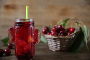 Berries and citrus infused water cocktail, compote, lemonade or tea. Summer iced cold drink with berries, cherry, lemon on a wooden rustic background with branch of cherry. With copy space for text.