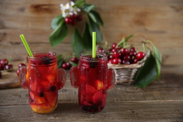 sweet compote of fresh berries and fruits in a glass jar with a straw for drinking with fresh berries of sweet cherry in a basket on a table made of natural wood. Fresh summer drink. With copy space.