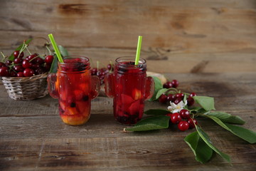 Berries and citrus infused water cocktail, compote, lemonade or tea. Summer iced cold drink with berries, cherry, lemon on a wooden rustic background with branch of cherry . With copy space for text.