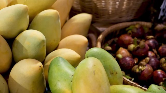 Fruits and vegetables on rustic stall. Assorted fresh ripe fruits and vegetables placed on rustic oriental stall in market. Green and yellow mango and mangosteens in basket