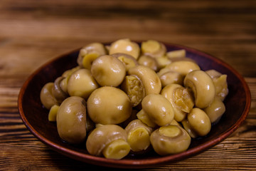 Ceramic plate with canned mushrooms on wooden table