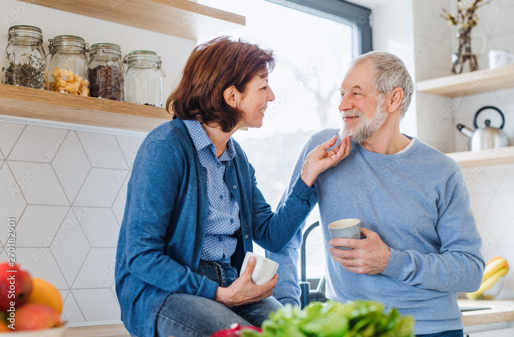 Wall mural a portrait of senior couple in love indoors at home, holding coffee.