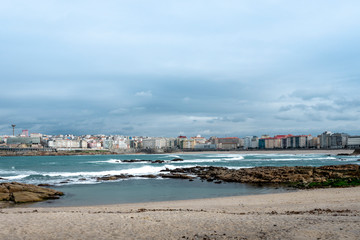 Fototapeta na wymiar View of the city of Coruña in Galicia Spain from the Riazor Beach with rocks on the shore with a cloudy sky 