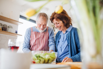 A portrait of senior couple in love indoors at home, cooking.