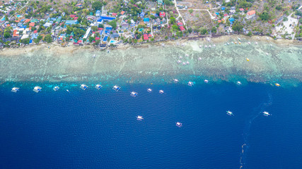 Aerial view of Filipino boats floating on top of clear blue waters, Moalboal is a deep clean blue ocean and has many local Filipino boats in the sea. Moalboal, Cebu, Philippines.