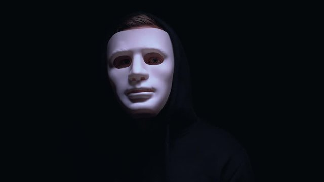 Man in terrible face mask staring at camera against dark background, terrorism
