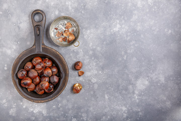 Roasted edible sweet chestnuts served in cast-iron skillet on gray background. Top view. Copy space.