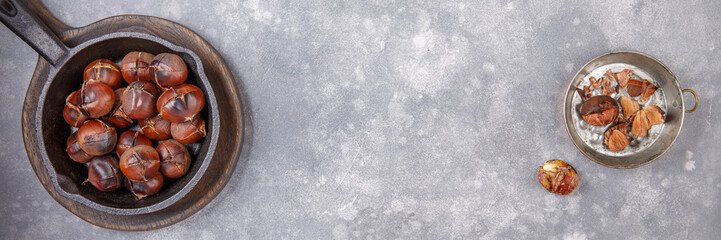 Roasted edible sweet chestnuts served in cast-iron skillet on gray background. Top view. Copy space.