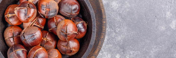 Roasted edible sweet chestnuts served in cast-iron skillet on gray background. Top view. Copy space.