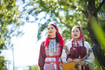 Two young women in traditional russian clothes walk holding hands and singing