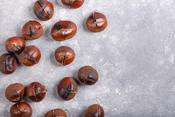 Obraz premium Heap of roasted edible sweet chestnuts on gray background. Top view. Copy space. Food background.