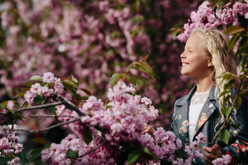 portrait of a beautiful little child girl with sakura flowers on a sunny spring day