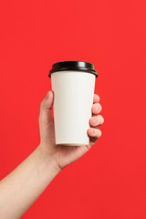 Paper cup of coffee or tea on a red background. Mockup of male hand holding paper cup isolated. Front view mockup of empty polystyrene coffee mug. Take away. Advertising coffee.