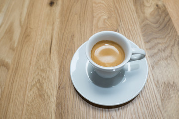 A white cup and saucer with coffee viewed from above on a wood patterned table top. 