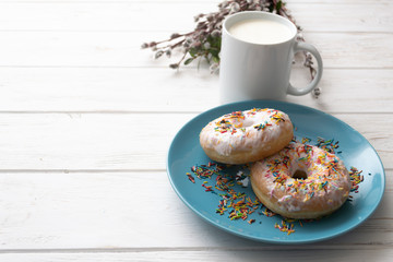 Donuts on a blue plate with a cup of milk on a white wooden background