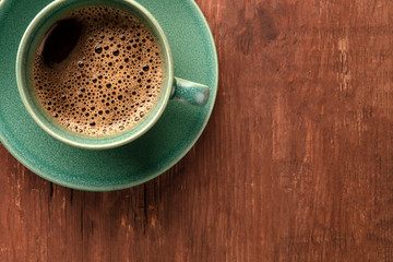 A closeup of a cup of black coffee on a dark rustic wooden background, shot from above with copyspace