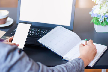 Young asian woman using smartphone and laptop working and write on note book to make an appointment