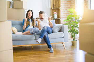 Young beautiful couple relaxing sitting on the sofa around boxes from moving to new house very...