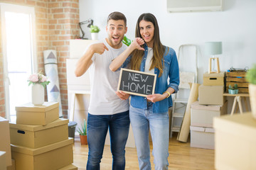 Fototapeta na wymiar Young beautiful couple holding blackboard with new home text at new house with surprise face pointing finger to himself