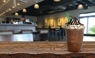 Frappuccino with cream and chocolate sauce in takeaway cup on wooden table at cafe