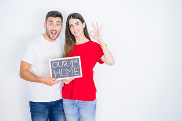 Young beautiful couple holding blackboard with new home text over white isolated background doing ok sign with fingers, excellent symbol