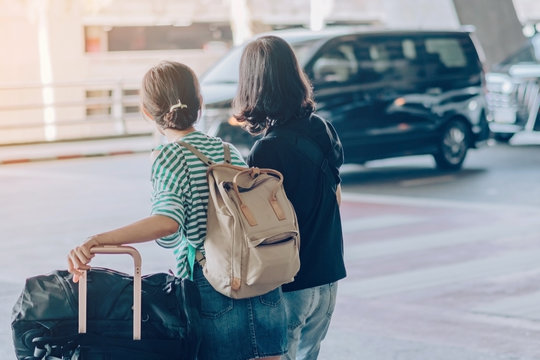 Passengers With Big Roller Luggage Stand To Wait For The Car To Pick Up At Airport Arrival Terminal.