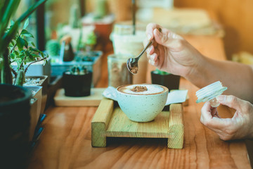 Woman pouring sugar into a white cup of coffee