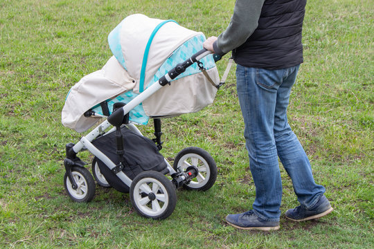 father walks with carriage, bottom view only legs. Bright mint stroller and legs in jeans, walking with a child outdoor