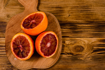 Obraz na płótnie Canvas Cutting board with halved sicilian oranges on a wooden table. Top view