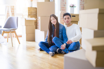 Fototapeta na wymiar Young asian couple sitting on the floor of new house arround cardboard boxes relaxing and smiling happy