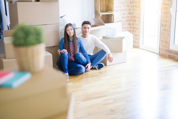 Young asian couple sitting on the floor of new house arround cardboard boxes relaxing and smiling happy